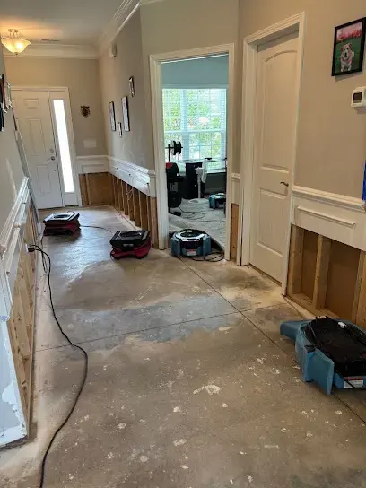 Air movers and a dehumidifier running in a room of a Cary home while a technician logs moisture readings