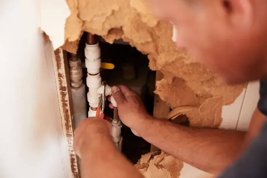 Plumber reaching into an opened wall cavity to reach a failed supply pipe fitting
