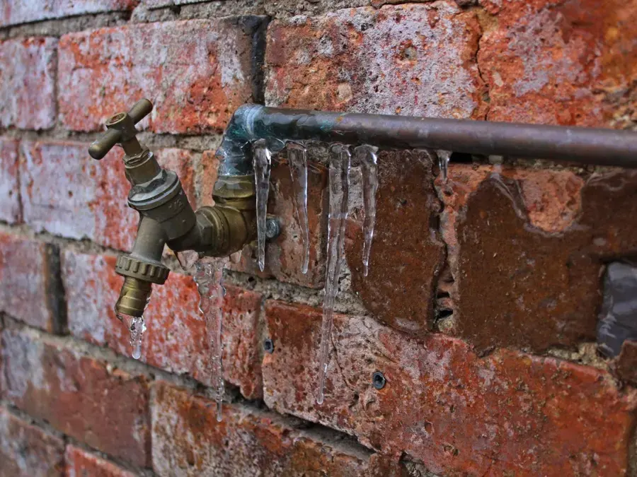 Outdoor hose spigot on a brick wall coated in ice during a hard freeze