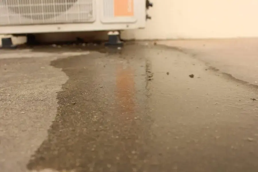 Water spreading across a concrete floor from beneath an air conditioning unit
