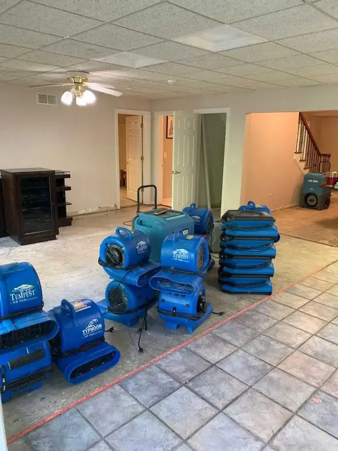 Stacks of blue air movers and dehumidifiers staged on a tile floor for structural drying