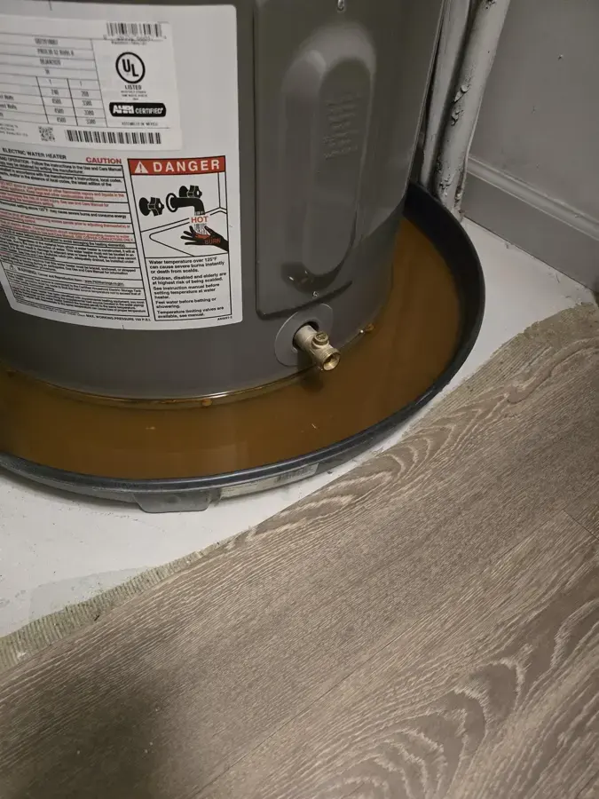 Base of a tank water heater sitting in a drain pan that holds rusty water